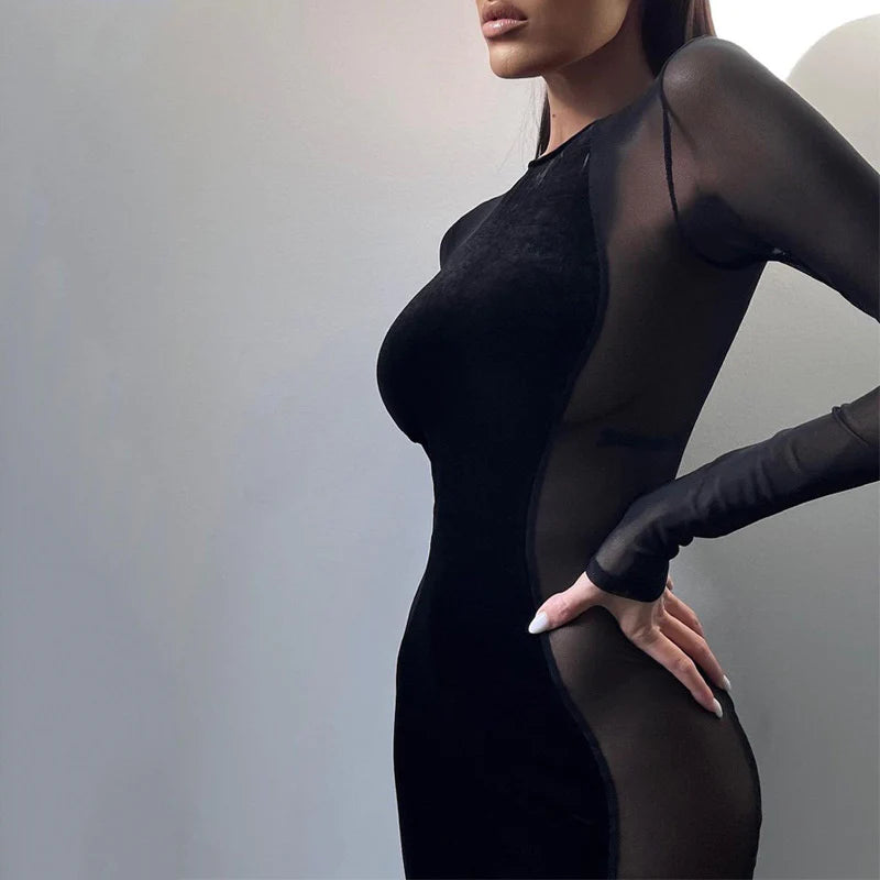 the model is wearing a long black dress with a mesh side see through sides with long mesh sleeves. The dress is form fitted and knee length